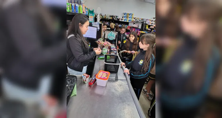 A proposta consistia em cada alunos levar um valor em dinheiro, algo simbólico, para a turma realizar compras coletivas e experienciar na prática os conceitos estudados.