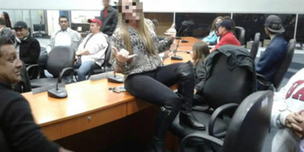 Imagem mostra mulher sentada na mesa e com o pé na cadeira durante um evento na Câmara de Ponta Grossa