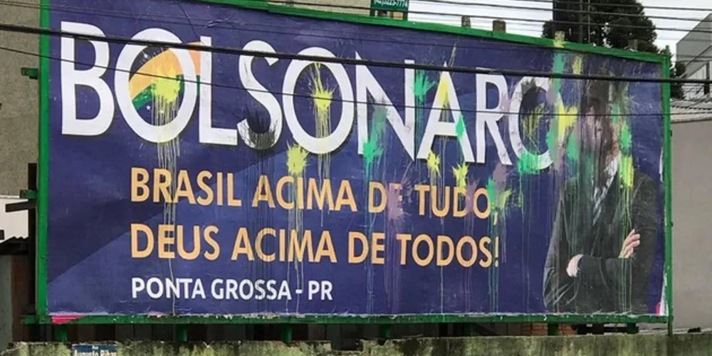 A placa, com os dizeres ‘Bolsonaro Brasil acima de tudo, Deus acima de todos!’, está manchada com as cores verde e amarelo. 
