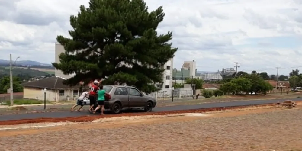 Foto mostra um grupo de pessoas empurrando um Gol, na pista de caminhada