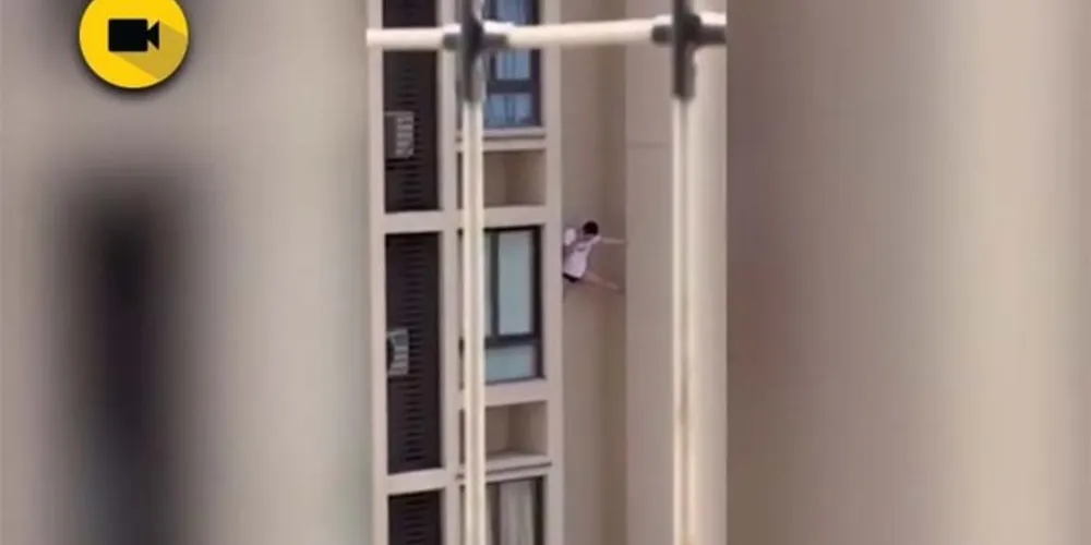 Jovem tenta se segurar com as costas contra a parede e uma perna aberta contra uma coluna de concreto

