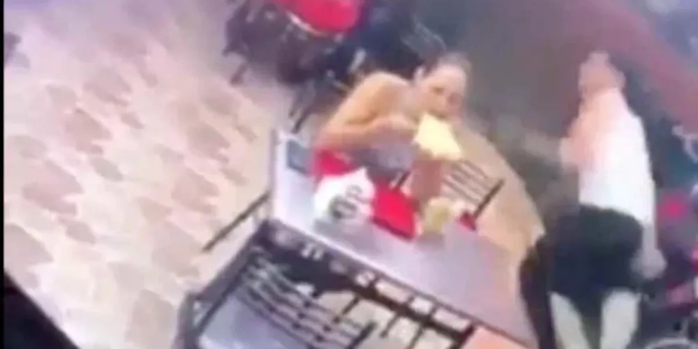 A mulher, sem perder a calma, entrega todos os pertences dela e do companheiro, que sai correndo ao perceber a ação dos criminosos no local.