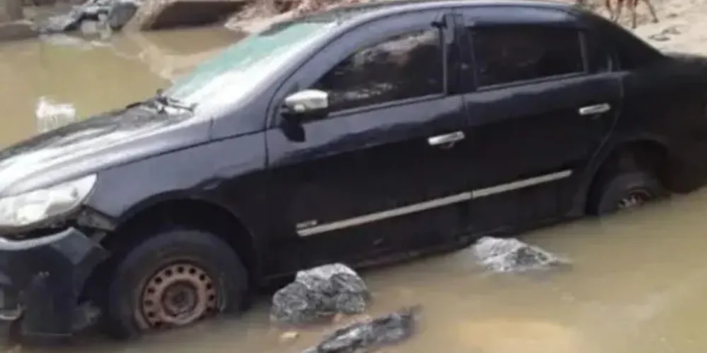 O carro estava parado sobre o córrego que cruza a estrada, com os vidros fechados.