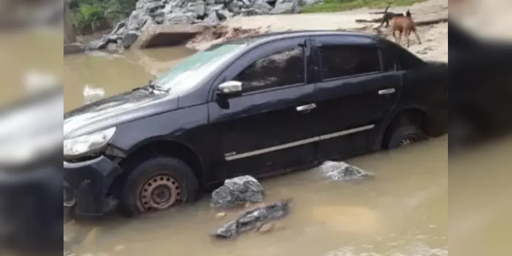 O carro estava parado sobre o córrego que cruza a estrada, com os vidros fechados.