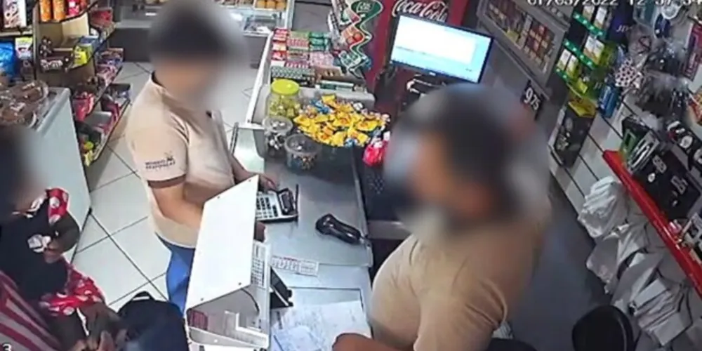 Nas imagens, é possível ver o momento em que um homem, armado com uma faca e segurando uma criança nos braços, entra no estabelecimento e anuncia o assalto.