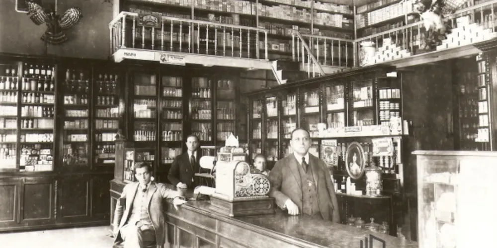 Interior da Farmácia e Drogaria Central. Na parte superior da fotografia pode-se perceber uma propaganda do "Biotônico Fontoura". Homens não identificados.