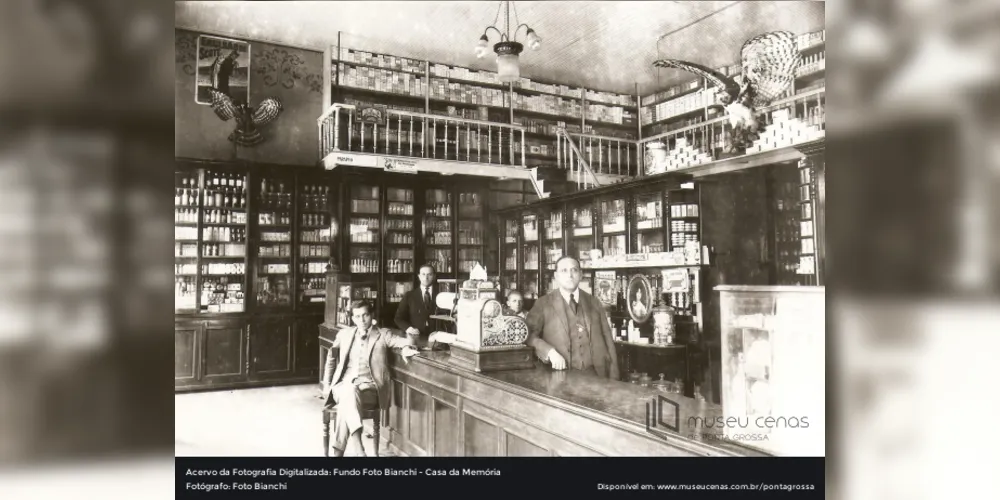 Interior da Farmácia e Drogaria Central. Na parte superior da fotografia pode-se perceber uma propaganda do "Biotônico Fontoura". Homens não identificados.