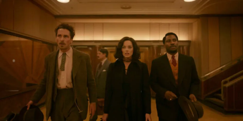 'Amsterdam' é um filme satisfeito consigo mesmo, não apenas satisfeito com a óbvia importância do seu tema político, mas satisfeito com as caricaturas que coloca em cena, com os rostos do seu belo elenco, com o sorriso sinistro de Bale, com a cadência envolvente da voz grave de Washington, com os leves movimentos de pescoço de Robbie