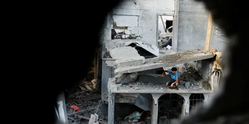 Um menino palestino sentado em uma casa danificada vista através dos escombros, após os ataques israelenses, em Khan Younis, no sul da Faixa de Gaza, 11 de outubro de 2023