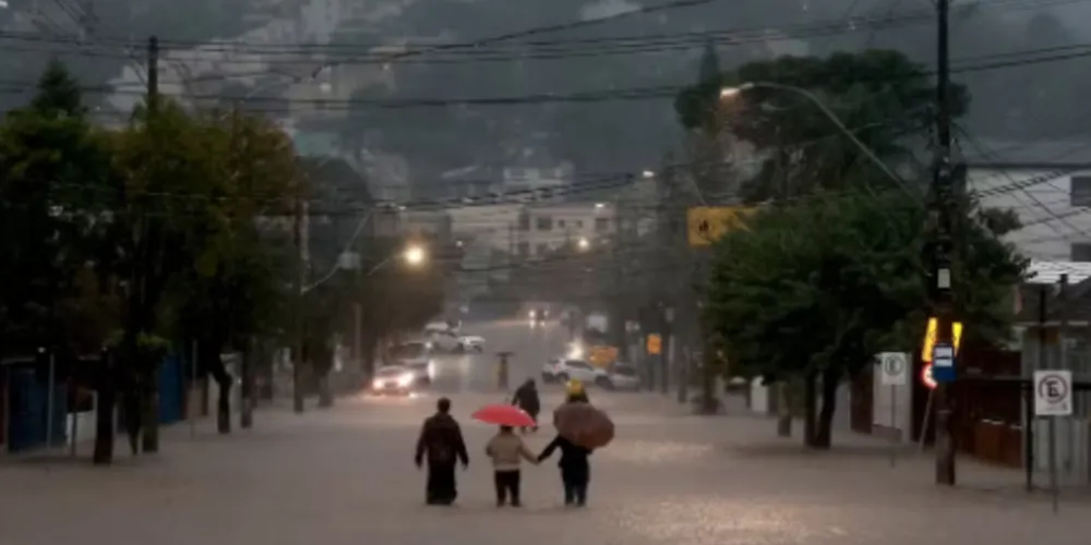 Pessoas caminham em rua alagada em bairro de Porto Alegre em 24 de maio de 2024