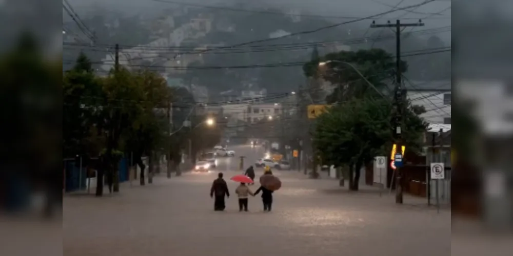 Pessoas caminham em rua alagada em bairro de Porto Alegre em 24 de maio de 2024