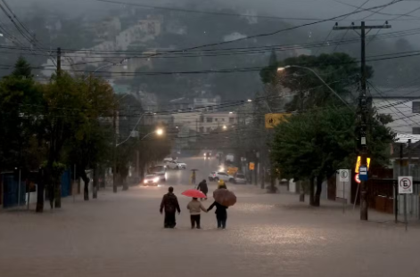 Pessoas caminham em rua alagada em bairro de Porto Alegre em 24 de maio de 2024