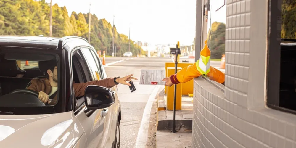 Colaborador da CCR PRVias entrega a motorista um folheto com orientações sobre início da cobrança de pedágio durante operação pré-assistida