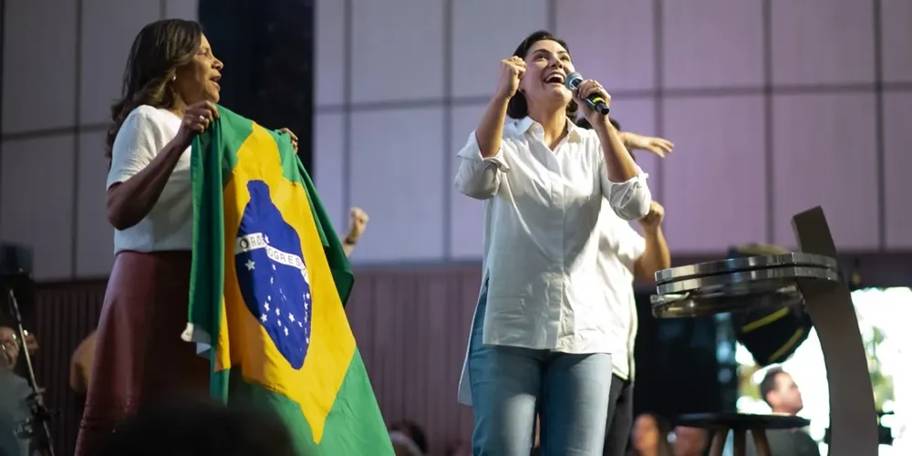 Michelle Bolsonaro ao lado da bandeira do Brasil