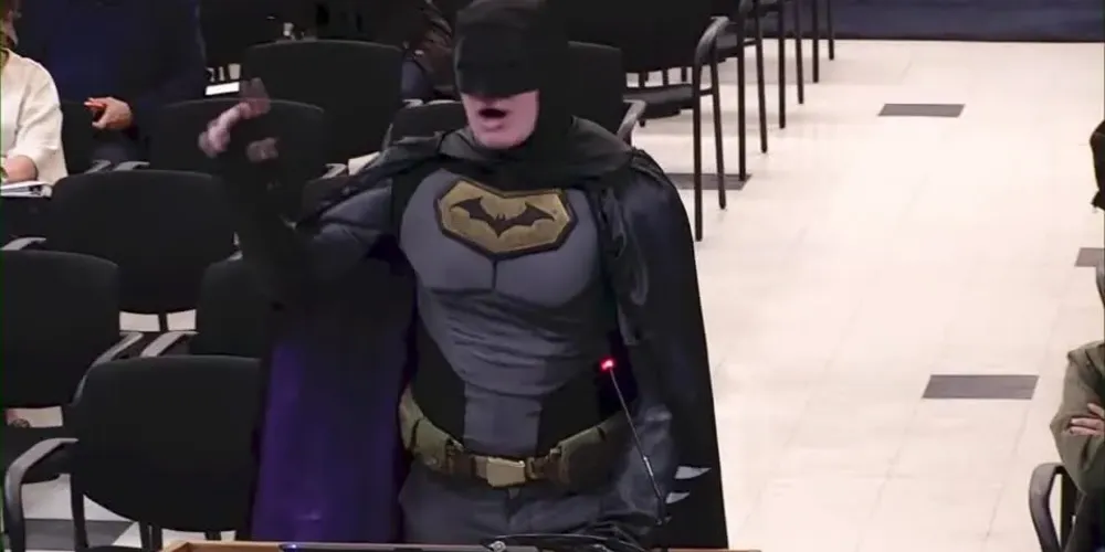 Homem fantasiado de Batman discursando em reunião do conselho municipal nos EUA