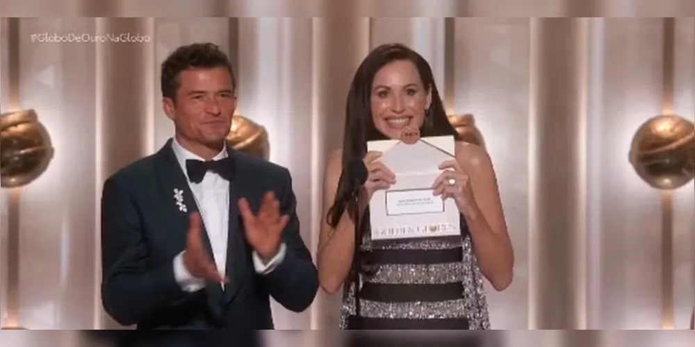 Mini Driver e Orlando Bloom anunciando 'O agente secreto' como vencedor do Globo de Ouro