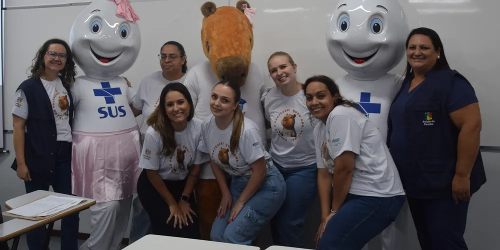 Profissionais posando para fotos junto com mascotes da saúde, incluindo o Zé Gotinha