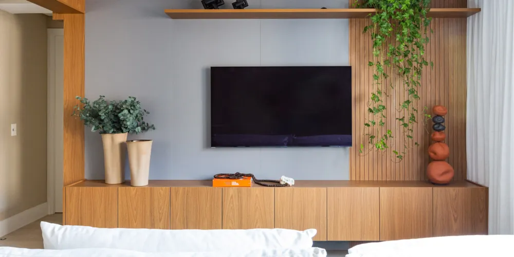 Deixando o painel de madeira do rack ainda mais aconchegante, uma espécie foi disposta pela arquiteta Daniela Funari na prateleira superior. O ripado lateral acolhe os ramos, entregando uma sala de estar muito mais acolhedora