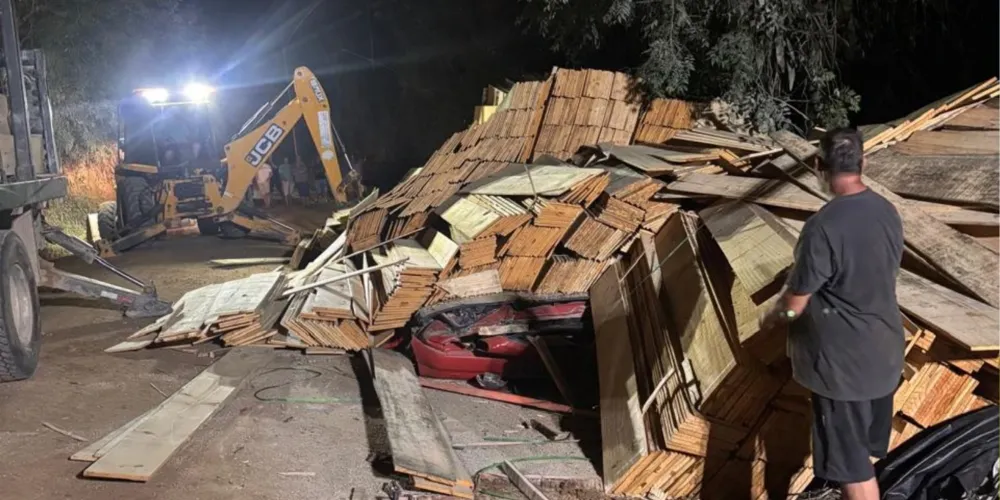 Carreta carregada com madeira tombada sobre carro