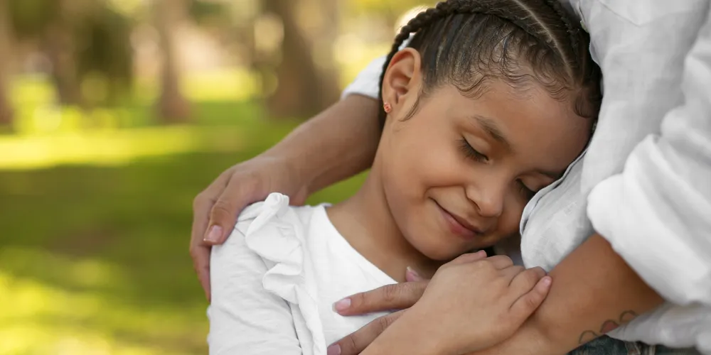 A imagem ilustra uma menina sendo protegida por uma pessoa adulta em um abraço