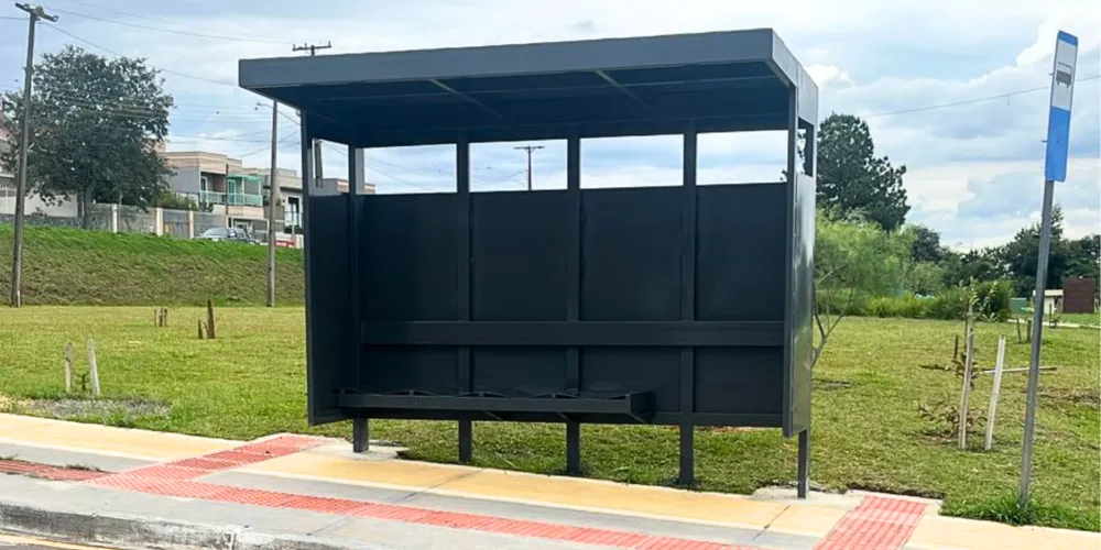 Na imagem, um ponto de ônibus em frente à um terreno