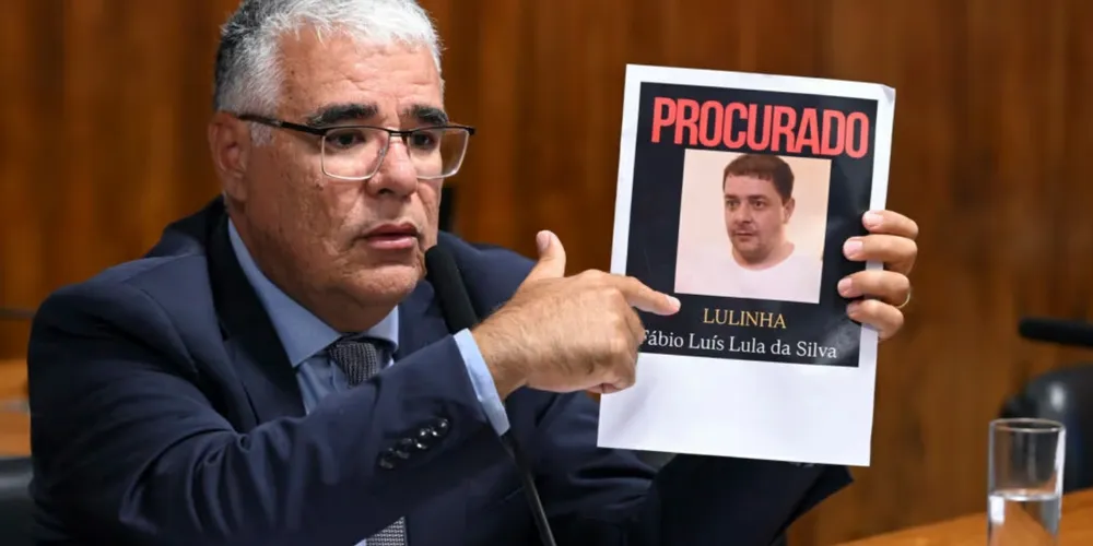 Eduardo Girão (Novo-CE), senador segurando um cartaz de 'Lulinha' durante a 'CPMI do INSS'