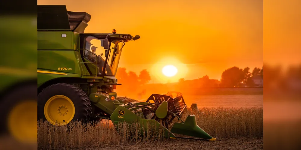 Henry County, Ohio - September 25, 2020: A profile view of a John Deere S670 harvesting soybeans during a hazy sunset with a red and orange sky from the bean dust.