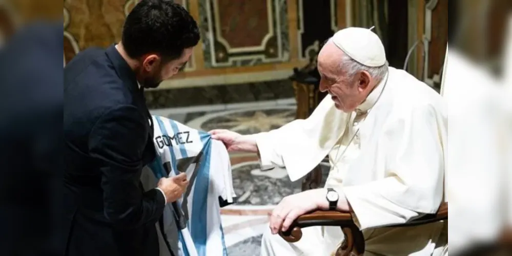 Papa segura o uniforme e olha atentamente para o objeto
