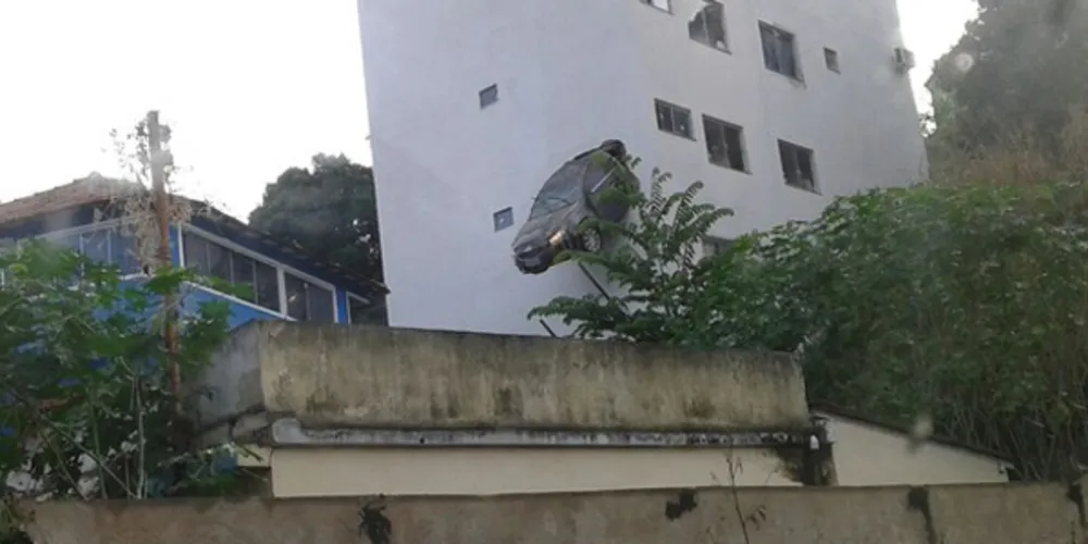 Imagem ilustrativa da imagem Carro quebra parede de prédio e fica pendurado